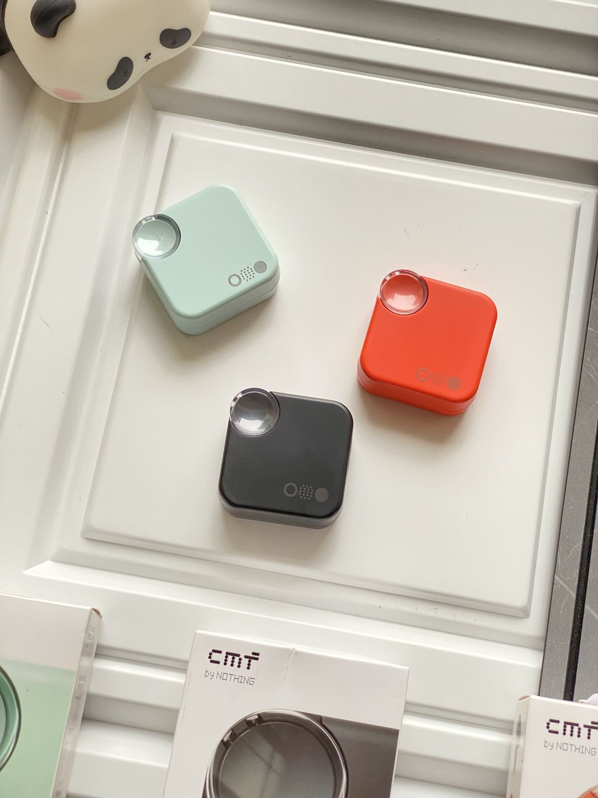 Three small electronic devices in green, red, and black on a white surface with 'CMT' branding visible.