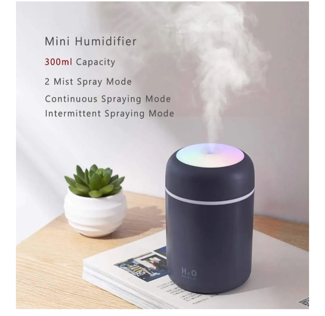 Mini humidifier with mist being emitted, placed on a table with a plant and newspaper.