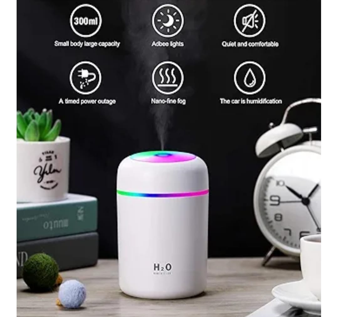 White humidifier with colorful light on a wooden surface, surrounded by books and a clock.