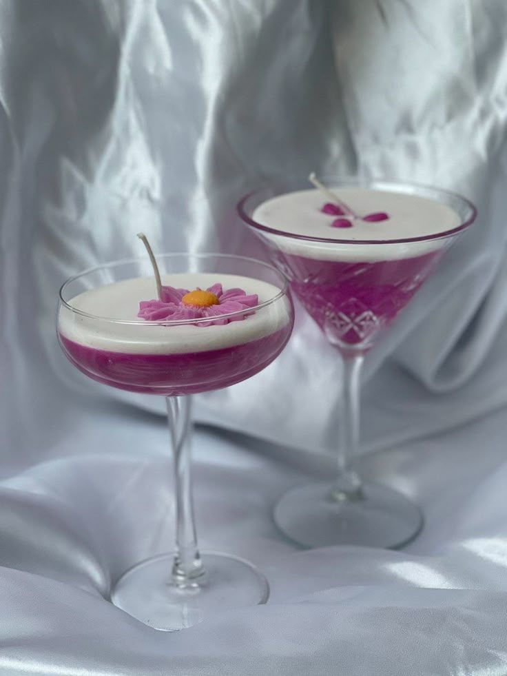 Two cocktail-shaped candles with floral decorations on a white fabric background