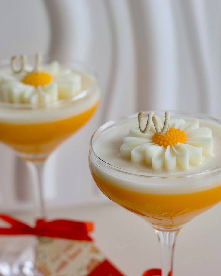 Two glasses of dessert with a floral topping on a white background