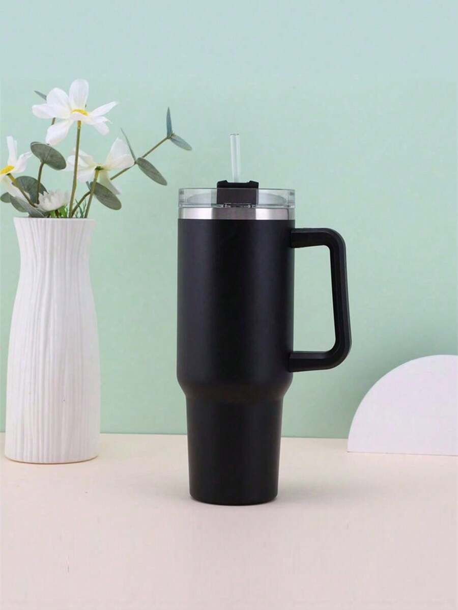 Black insulated mug with handle on a light surface against a light green background
