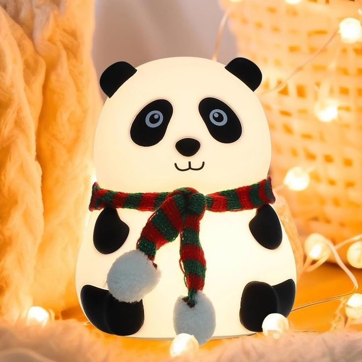 Cute panda-shaped night light with a red and green scarf on a warm, blurred background.