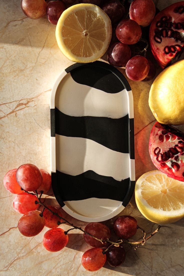 Black and white striped ceramic plate with lemons and grapes on a marble surface