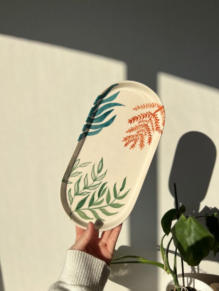 Hand holding a decorative plate with leaf patterns against a neutral background