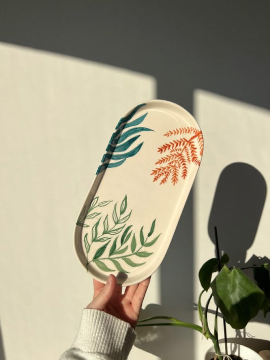 Hand holding a decorative plate with leaf patterns against a neutral background