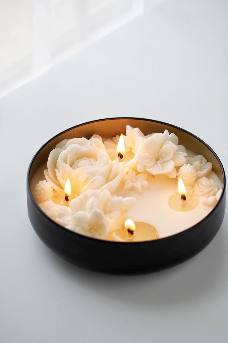 Decorative candle with floral design in a black bowl on a white background
