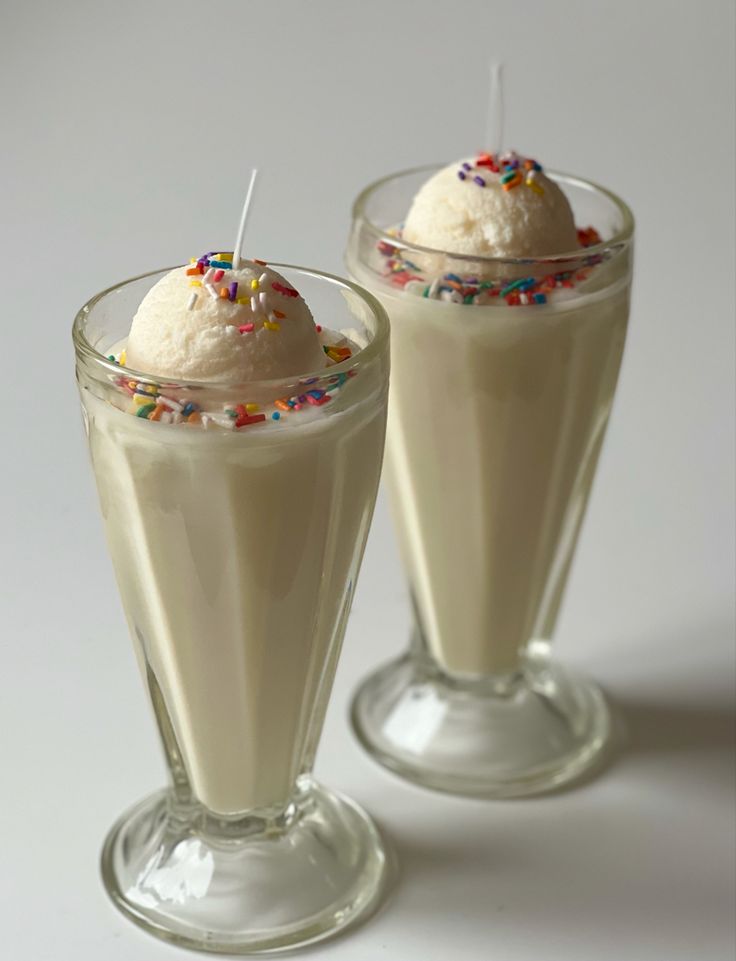 Two milkshakes with ice cream and sprinkles on a white background