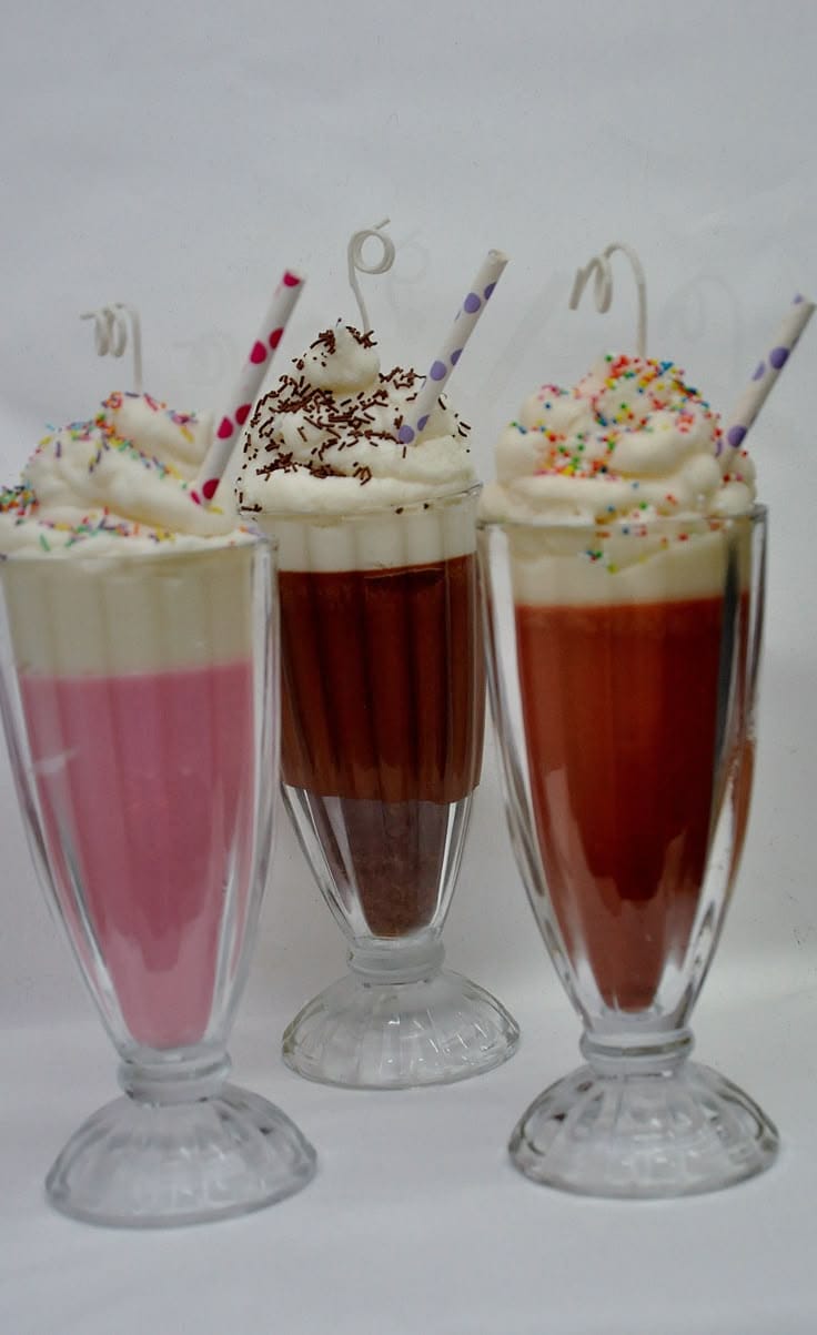 Three layered dessert drinks with whipped cream and sprinkles on a white background