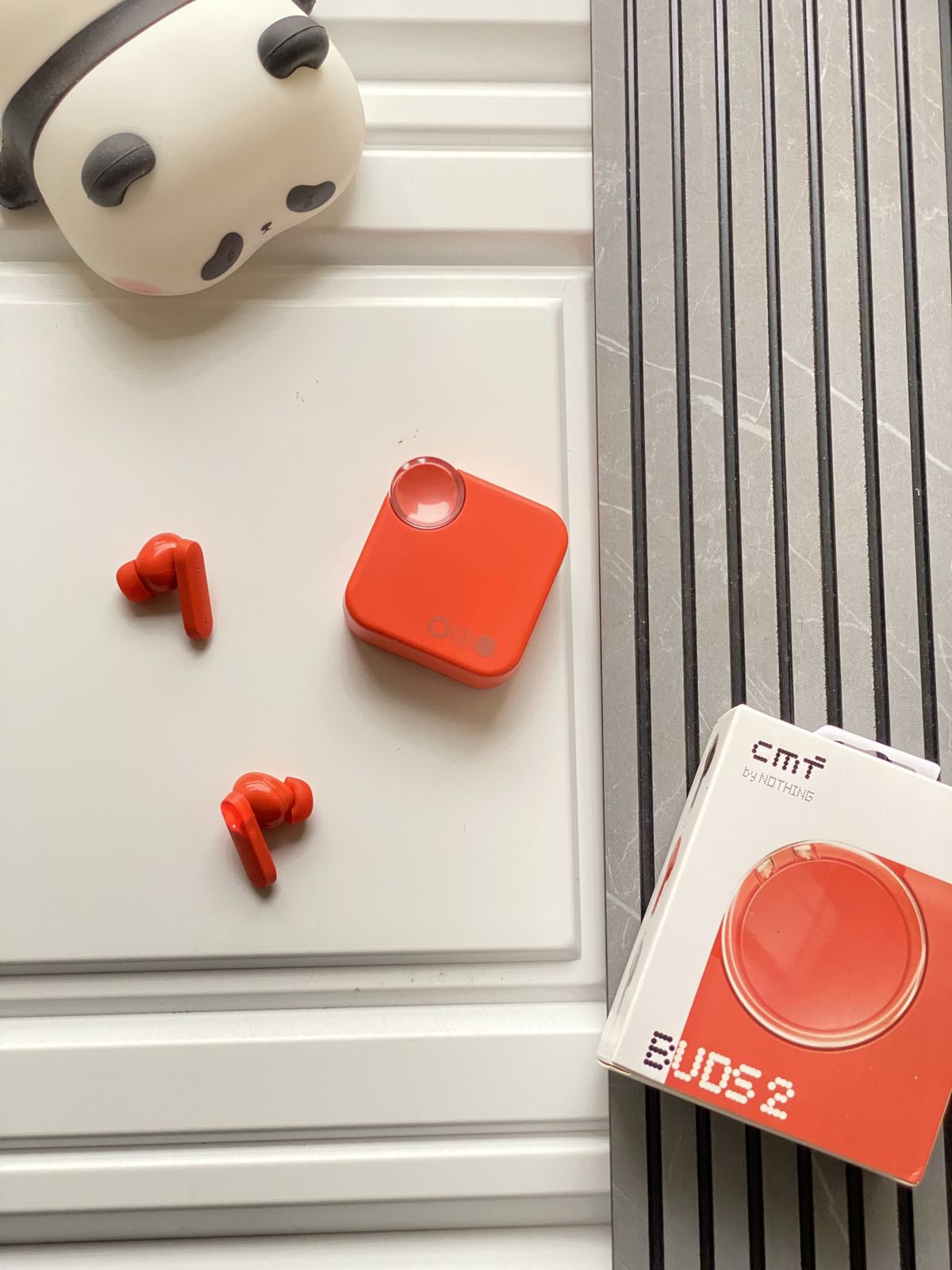 Red wireless earbuds with charging case on a white surface next to a box labeled 'Buds 2'.